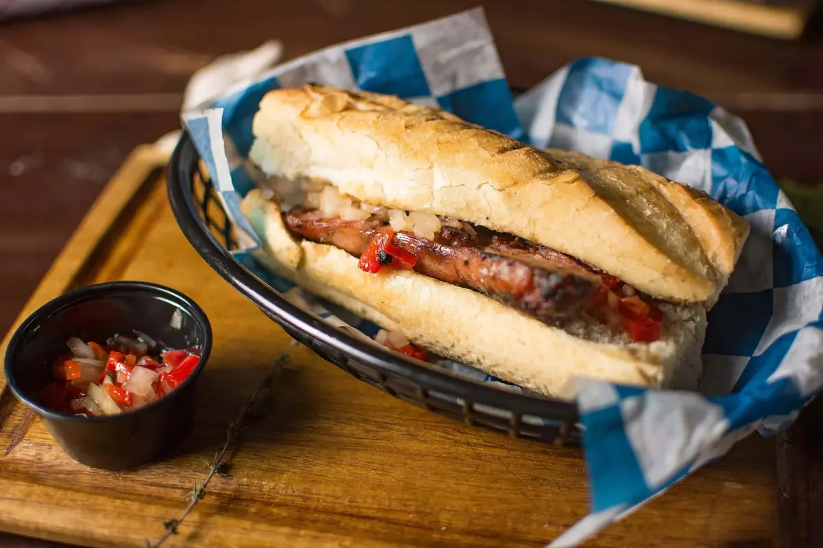 Choripán servido en un pan con salsa criolla